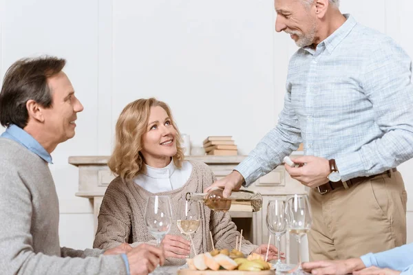 Homem mais velho com garrafa na mão de pé contra o marido sentado e esposa — Fotografia de Stock