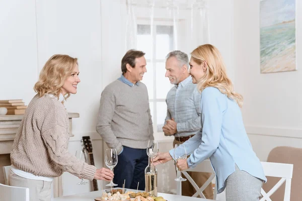 Fröhliche Freunde, die reden und Getränke trinken, während sie im Zimmer gegen den Tisch stehen — Stockfoto