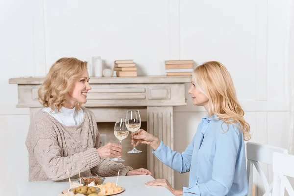 Women cheering with glasses in hands while sitting at table — Stock Photo
