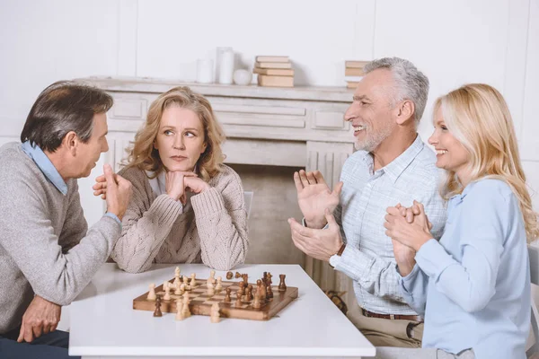 Amigos sentados à mesa com mesa de xadrez no interior do quarto — Fotografia de Stock