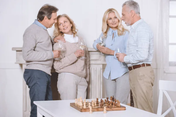Amigos felizes falando e segurando óculos em mãos contra mesa com mesa de xadrez — Fotografia de Stock