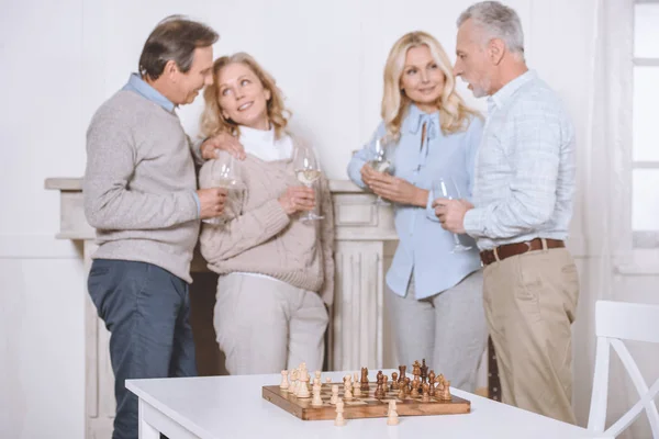 Amis heureux parlant et tenant des lunettes dans les mains contre la table avec bureau d'échecs — Photo de stock