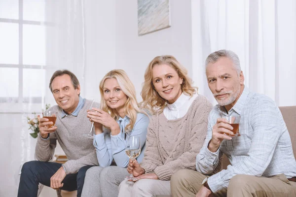 Amici felici con gli occhiali in mano seduti sul divano e guardando la fotocamera — Foto stock