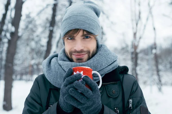 Jeune homme tenant une tasse de café chaud dans les mains dans le parc d'hiver — Photo de stock