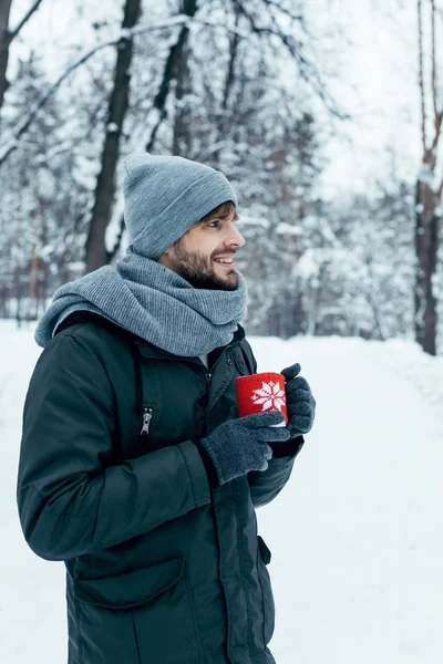 Young man holding cup of hot coffee in hands in winter park — Stock Photo