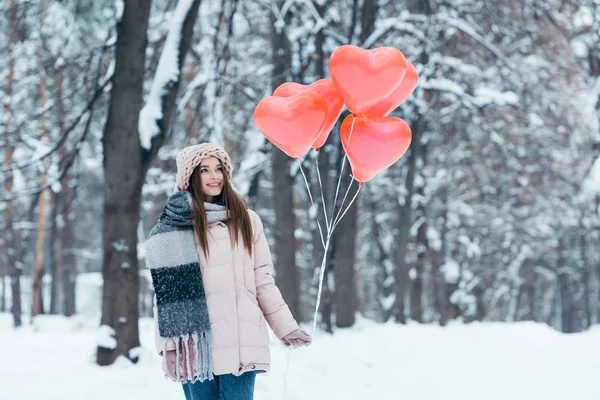 Портрет красивої молодої дівчини з повітряними кулями у формі серця в зимовому парку — стокове фото