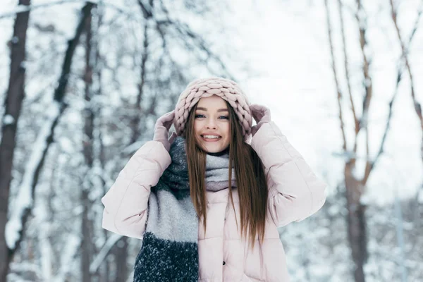 Portrait d'une femme souriante vêtue d'hiver regardant une caméra dans un parc enneigé — Photo de stock