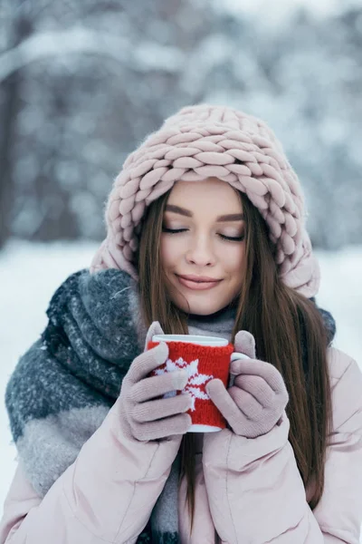 Ritratto di bella donna con gli occhi chiusi e tazza di caffè caldo in mano nel parco innevato — Foto stock