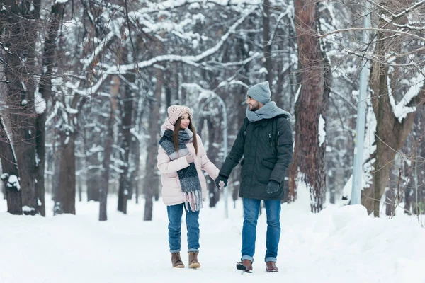 Junges lächelndes Paar hält Händchen und geht im Winterpark spazieren — Stockfoto