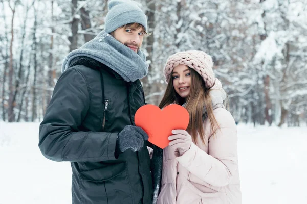 Portrait of young couple holding red heart in hands together in winter park — Stock Photo