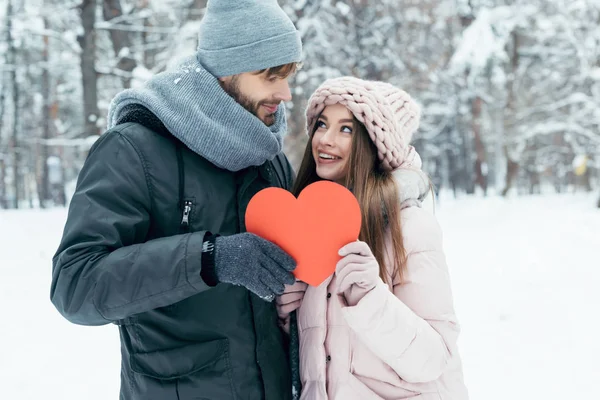 Ritratto di giovane coppia che tiene il cuore rosso tra le mani insieme nel parco invernale — Foto stock