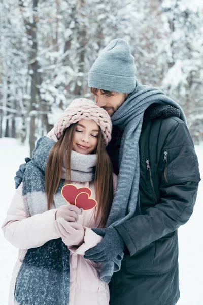 Casal macio com corações vermelhos no parque nevado no dia de inverno — Fotografia de Stock