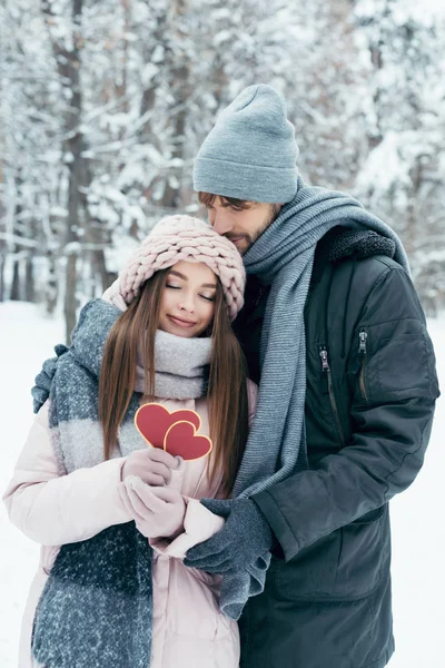 Tenera coppia con cuori rossi nel parco innevato nella giornata invernale — Foto stock