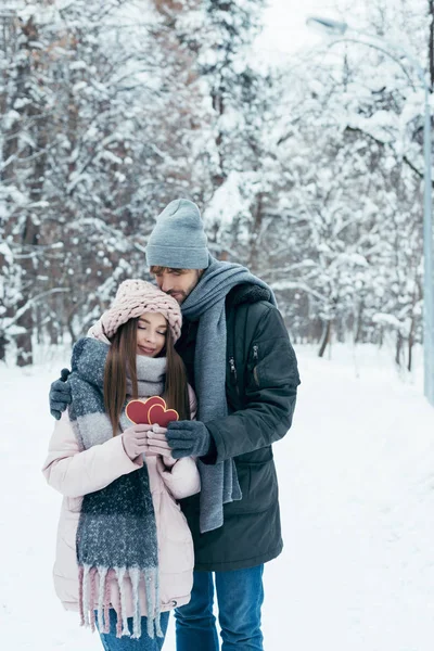 Casal macio com corações vermelhos no parque nevado no dia de inverno — Fotografia de Stock
