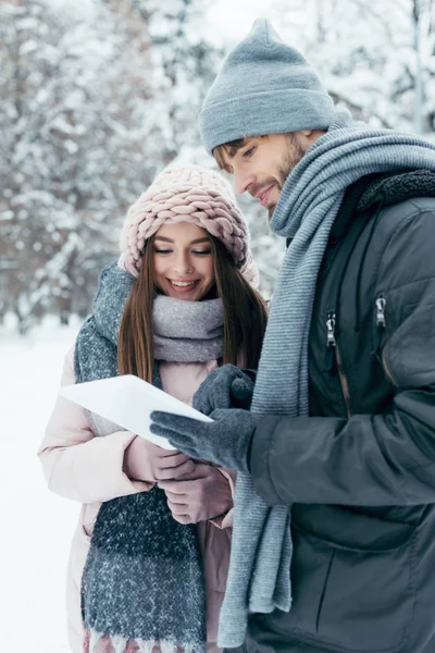 Портрет молодой счастливой пары с табличкой в снежном парке — стоковое фото
