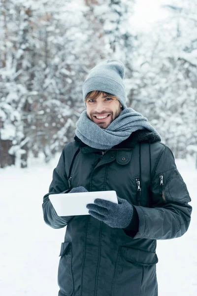 Porträt eines jungen lächelnden Mannes mit Tablet, der im Winterpark in die Kamera blickt — Stockfoto