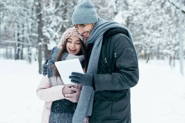 Retrato de pareja feliz joven con la tableta en el parque cubierto de nieve - foto de stock