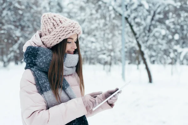 Seitenansicht einer lächelnden jungen Frau mit Tablet im Winterpark — Stockfoto