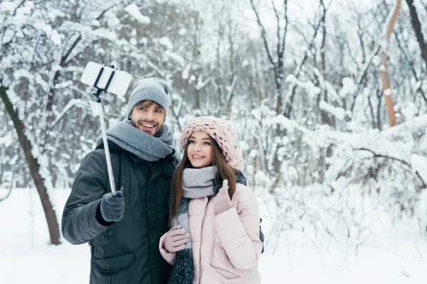 Smiling couple taking selfie together on smartphone in winter park — Stock Photo