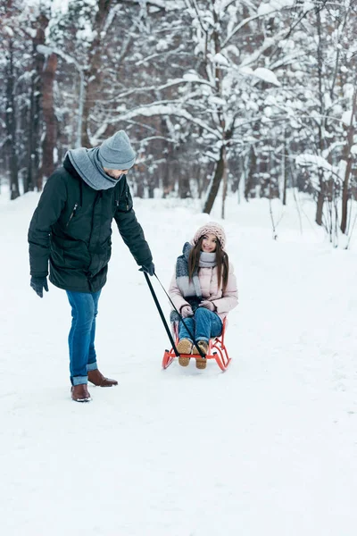 Молодая пара катается на санках в зимний день в парке — стоковое фото