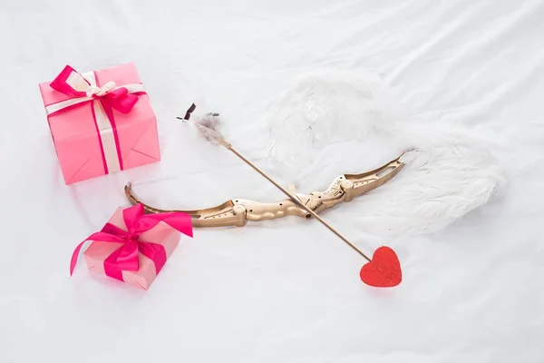 Vista superior de regalos, alas, arco y flecha en la cama - foto de stock