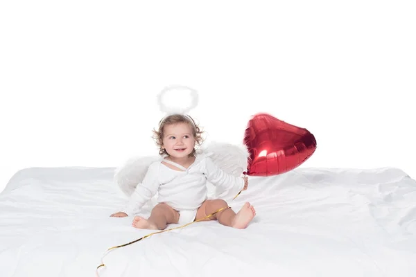 Маленький ангел с крыльями и нимбом, держащий красный сердечный шар, изолированный на белом — стоковое фото