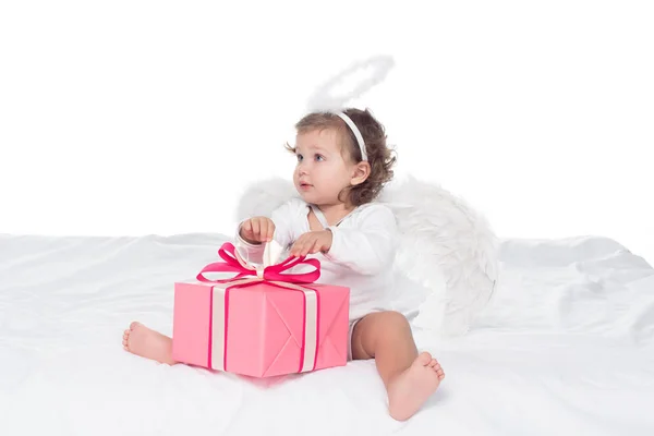 Little angel with nimbus sitting on bed with gift boxes, isolated on white — Stock Photo