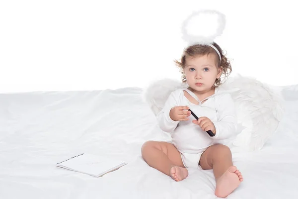 Маленький ангел з крилами і німбом на ліжку з блокнотом, ізольований на білому — стокове фото