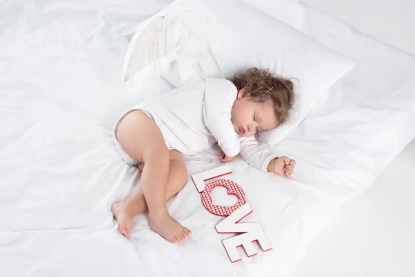 Little cherub with wings lying on bed with love sign — Stock Photo