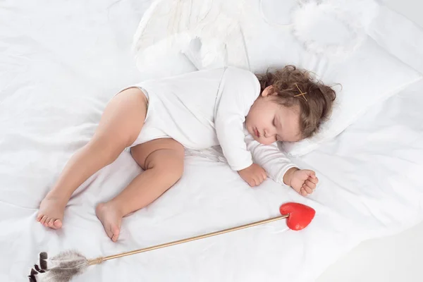 Petit Cupidon avec des ailes dormant sur le lit avec flèche — Photo de stock