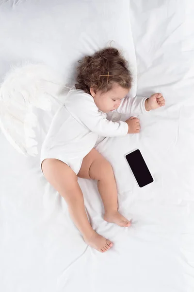 Маленький ангел спит на кровати со смартфоном — стоковое фото