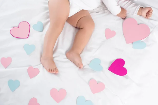 Cropped view of little baby lying on bed with hearts — Stock Photo