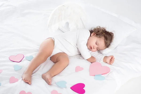Little cherub with wings sleeping on bed with hearts — Stock Photo