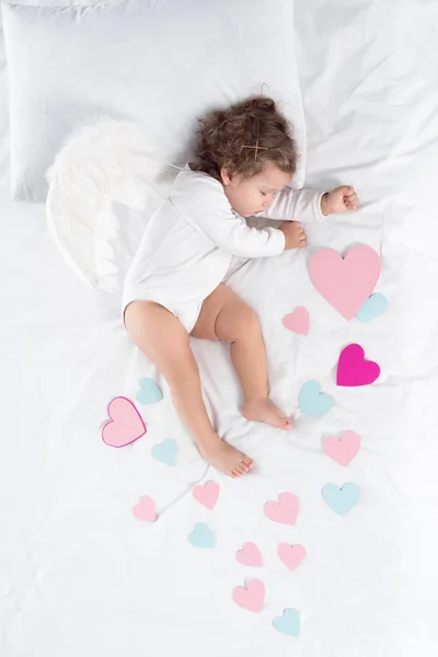 Cupid with wings sleeping on bed with hearts — Stock Photo