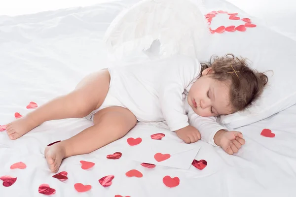 Маленький сонний херувими з крилами лежить на ліжку з серцями — стокове фото