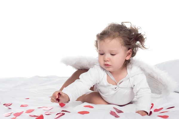 Petit Cupidon avec des ailes sur le lit avec des coeurs, isolé sur blanc — Photo de stock