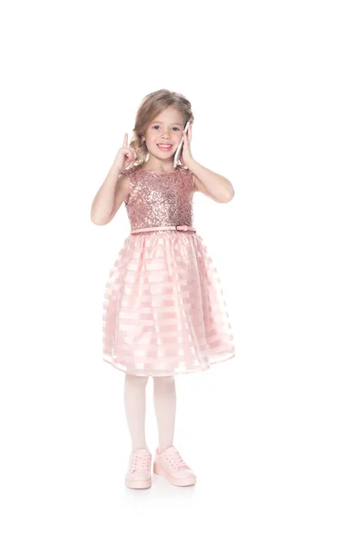 Усміхнена дитина вказує вгору під час розмови на смартфоні, ізольована на білому — стокове фото