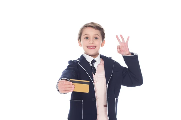 Piccolo ragazzo in possesso di carta di credito dorata e segno ok, isolato su bianco — Foto stock