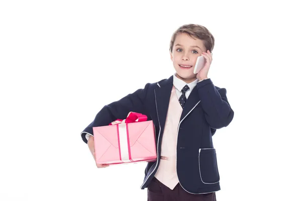 Lindo niño sonriente sosteniendo caja de regalo y hablando en el teléfono inteligente aislado en blanco - foto de stock