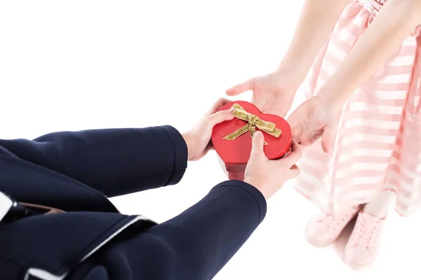 Cropped shot of boy in suit presenting heart shaped gift box to little girl in pink dress isolated on white — Stock Photo