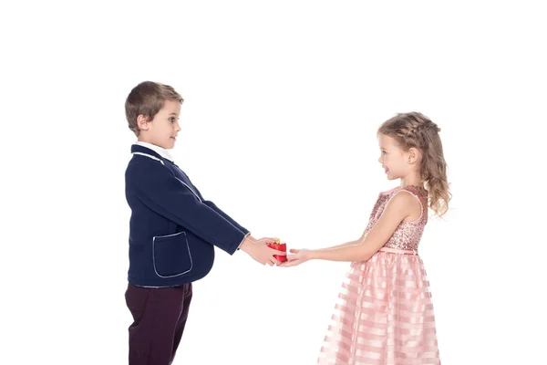 Vista lateral de adorables niños elegantes que sostienen la caja de regalo en forma de corazón aislada en blanco - foto de stock