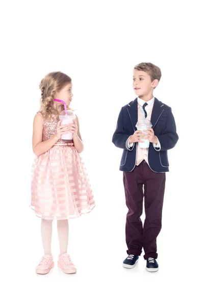Adorable fashionable little kids holding milkshakes in plastic cups and smiling each other isolated on white — Stock Photo
