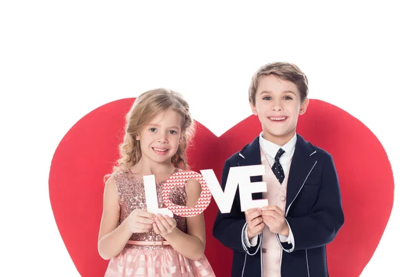 Lindos niños pequeños sosteniendo la palabra amor y sonriendo a la cámara aislada en blanco - foto de stock