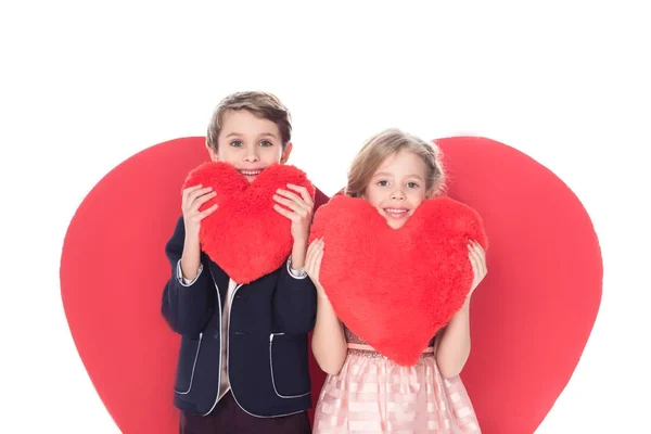 Cute little kids holding heart shaped pillows and smiling at camera isolated on white — Stock Photo