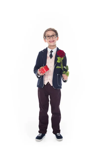 Menino bonito em terno e óculos segurando rosa flor e coração em forma de caixa de presente vermelho isolado no branco — Fotografia de Stock