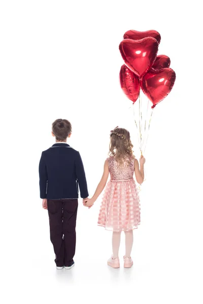 Вид ззаду милих маленьких дітей з повітряними кулями у формі серця, що тримають руки ізольовані на білому — стокове фото
