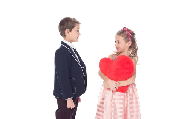 Smiling little boy looking at adorable girl holding red heart shaped pillow isolated on white — Stock Photo