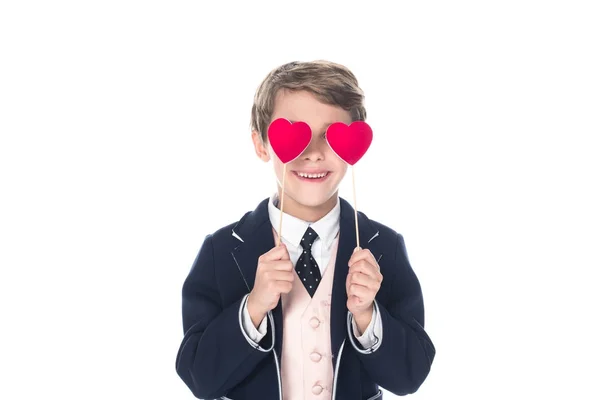 Lindo niño sonriente en traje sosteniendo corazones rojos en palos aislados en blanco - foto de stock