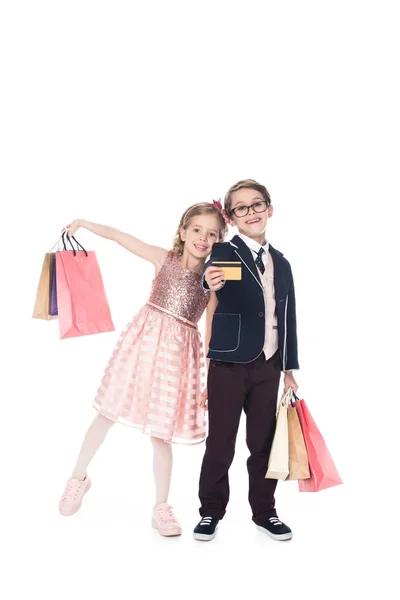 Niedliche modische Kinder mit Papiertüten und Kreditkarte lächeln in die Kamera isoliert auf weiß — Stockfoto