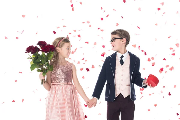 Прелестные счастливые дети с розами и сердечной формы подарочная коробка держа руки и улыбаясь друг другу на белом — стоковое фото